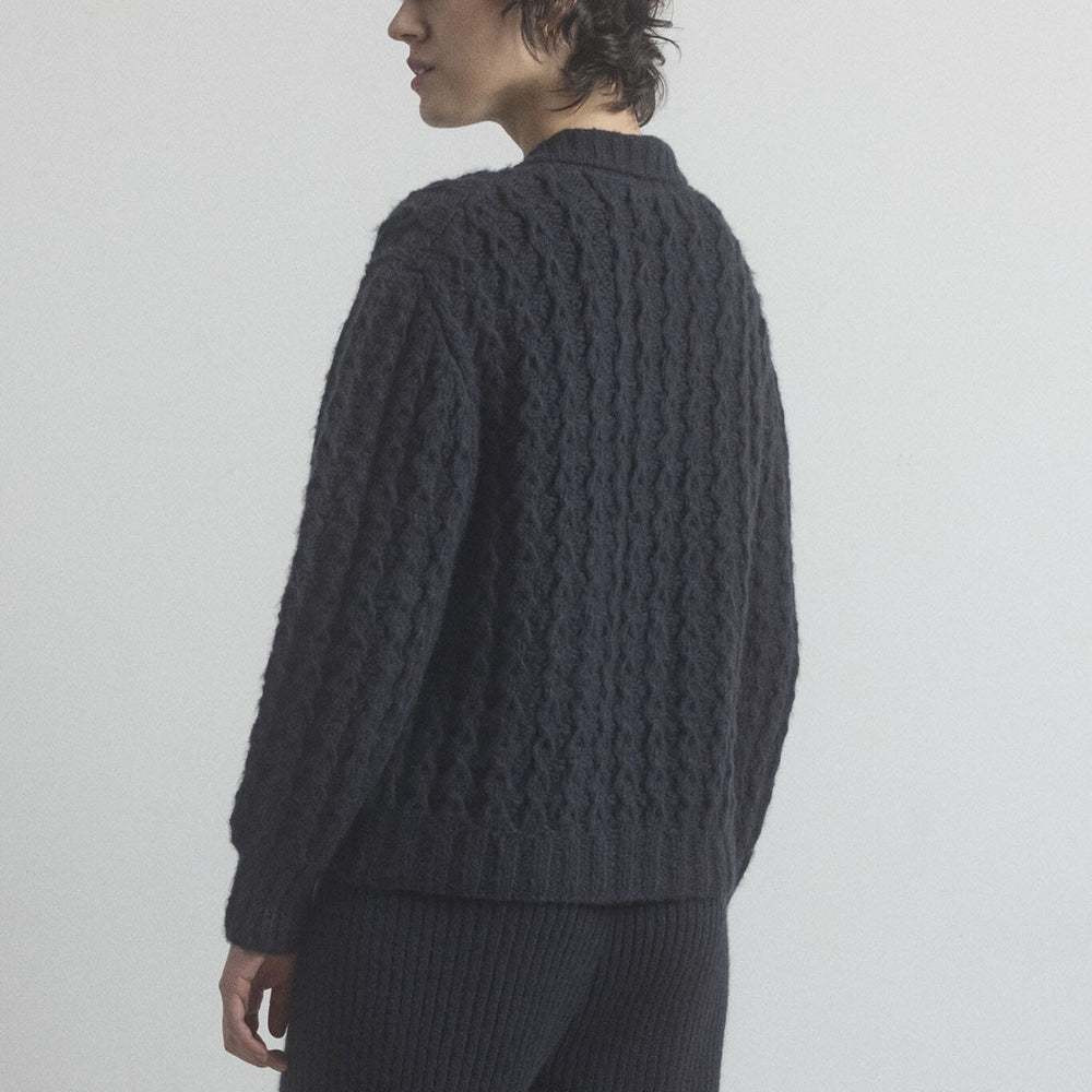 
                  
                    Person wearing a black cable knit sweater and pants on a plain background.
                  
                