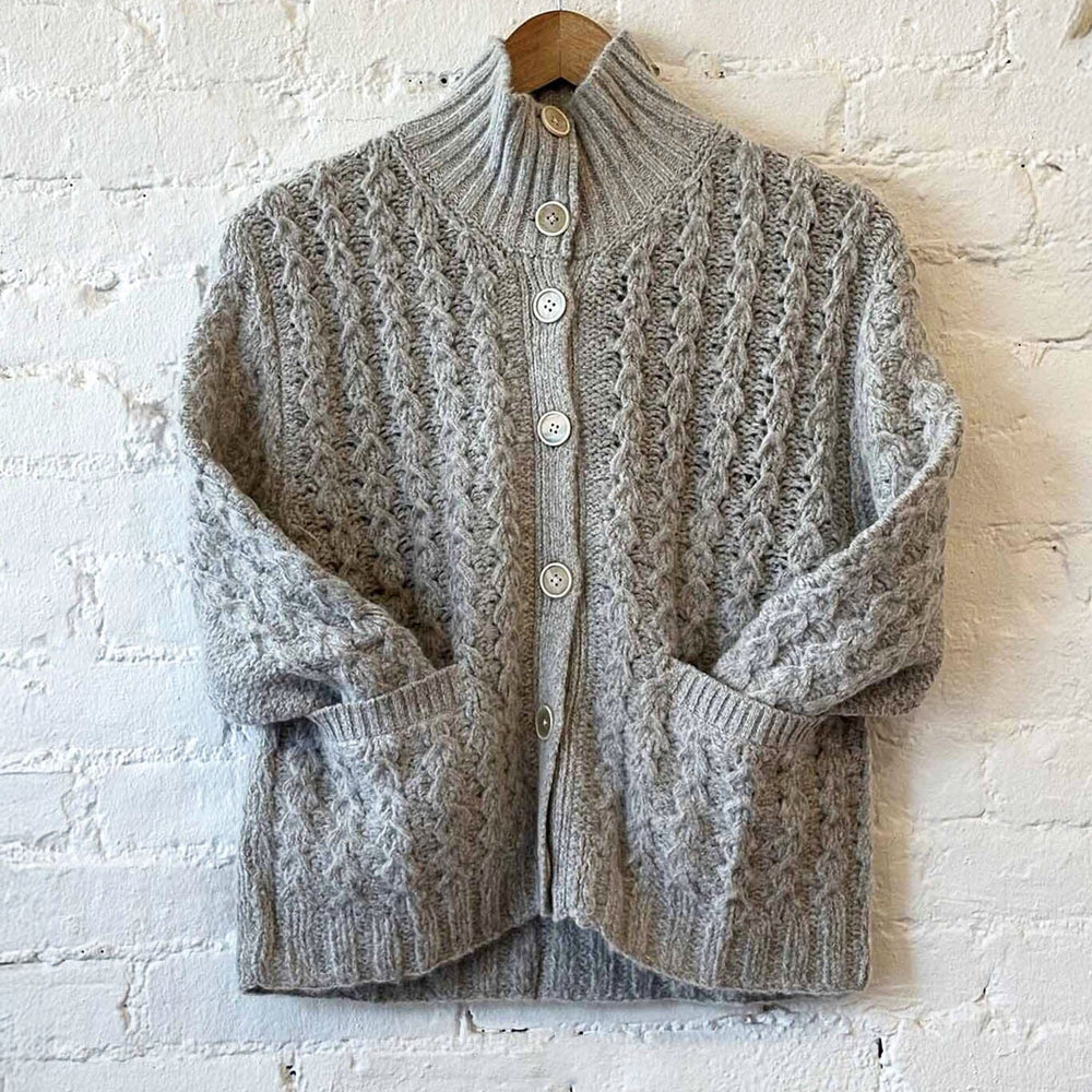 Gray knitted cardigan on a hanger against a white brick wall