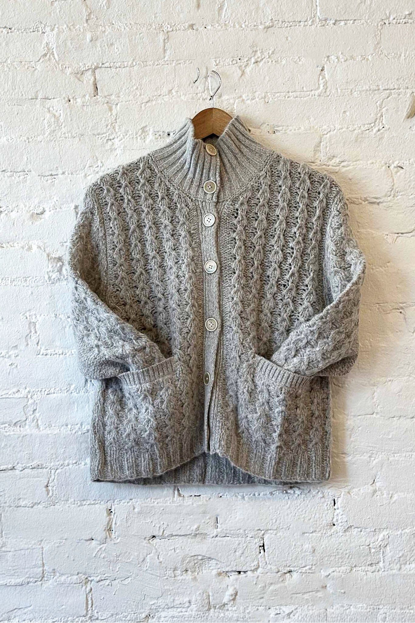 Gray knitted cardigan on a hanger against a white brick wall