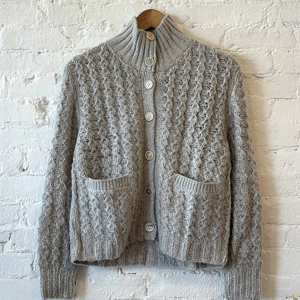 Gray knitted cardigan on a wooden hanger against a white brick wall.
