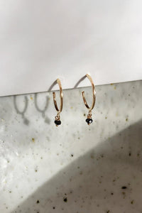 A pair of dainty gold hoops with black diamond beads.