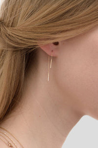 A close-up image of a woman's ear wearing a gold threader chain earring.
