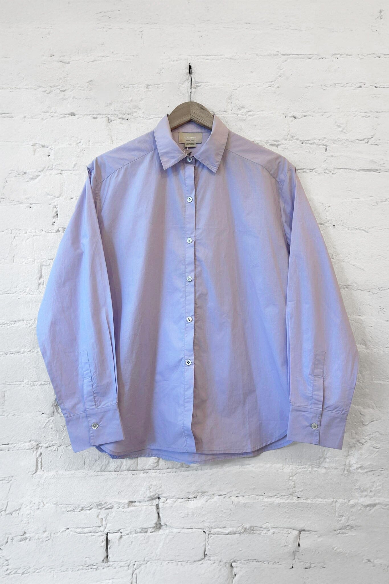 Light purple button-up shirt on a hanger against a white brick wall.