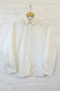 White button-up shirt on a wooden hanger against a white brick wall.