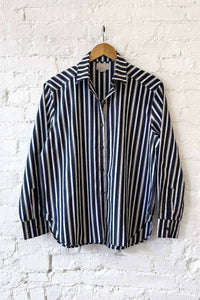 Navy and white striped long sleeve shirt on a hanger against a white brick wall.