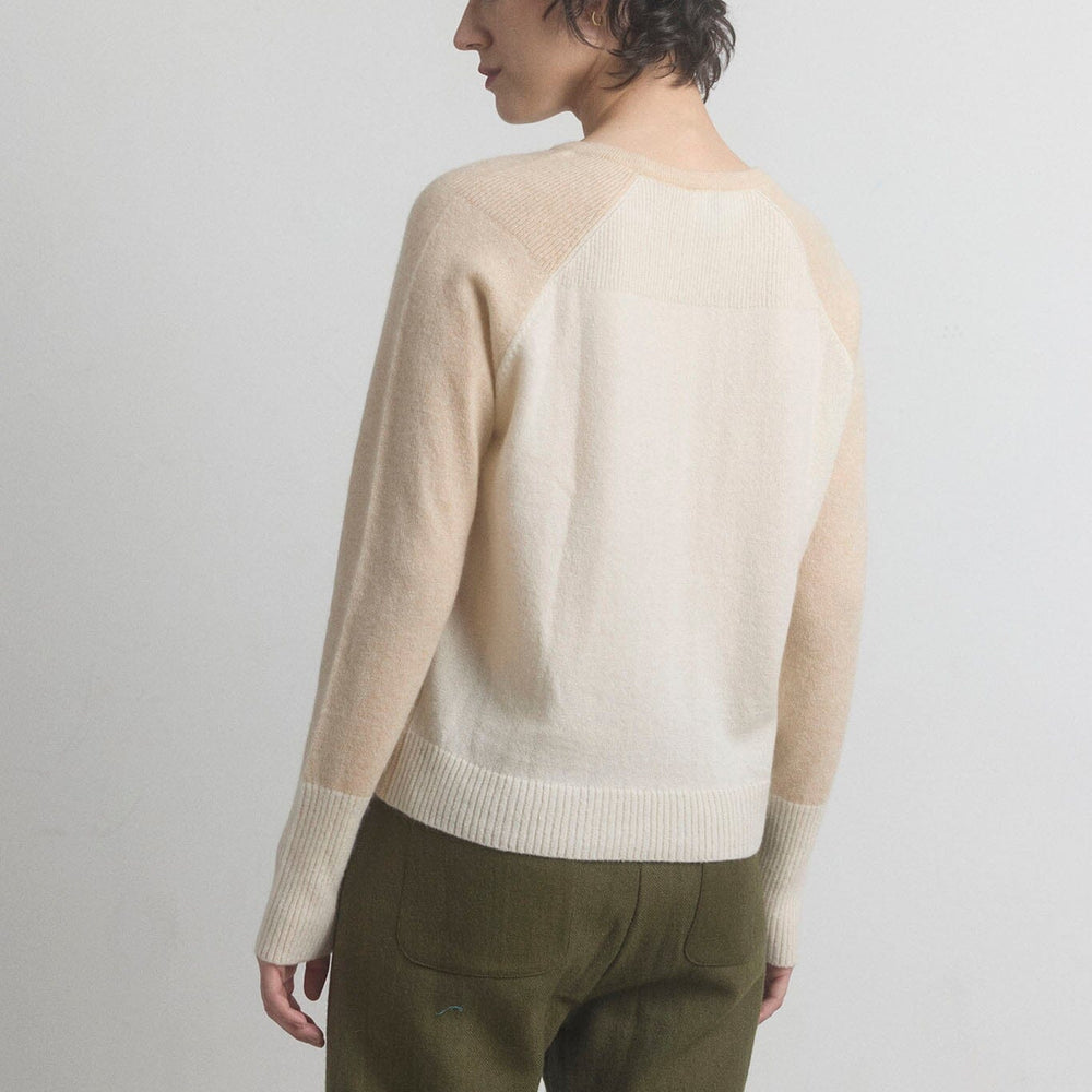 Woman showing the back of a beige cashmere sweater and green pants on a light gray background