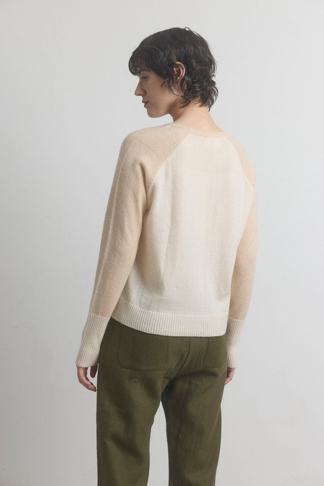 Woman showing the back of a beige cashmere sweater and green pants on a light gray background