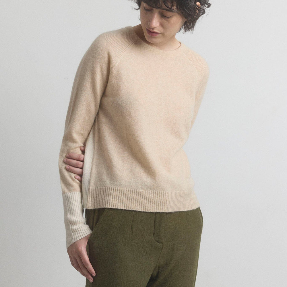Woman wearing a beige cashmere sweater and green pants on a light gray background