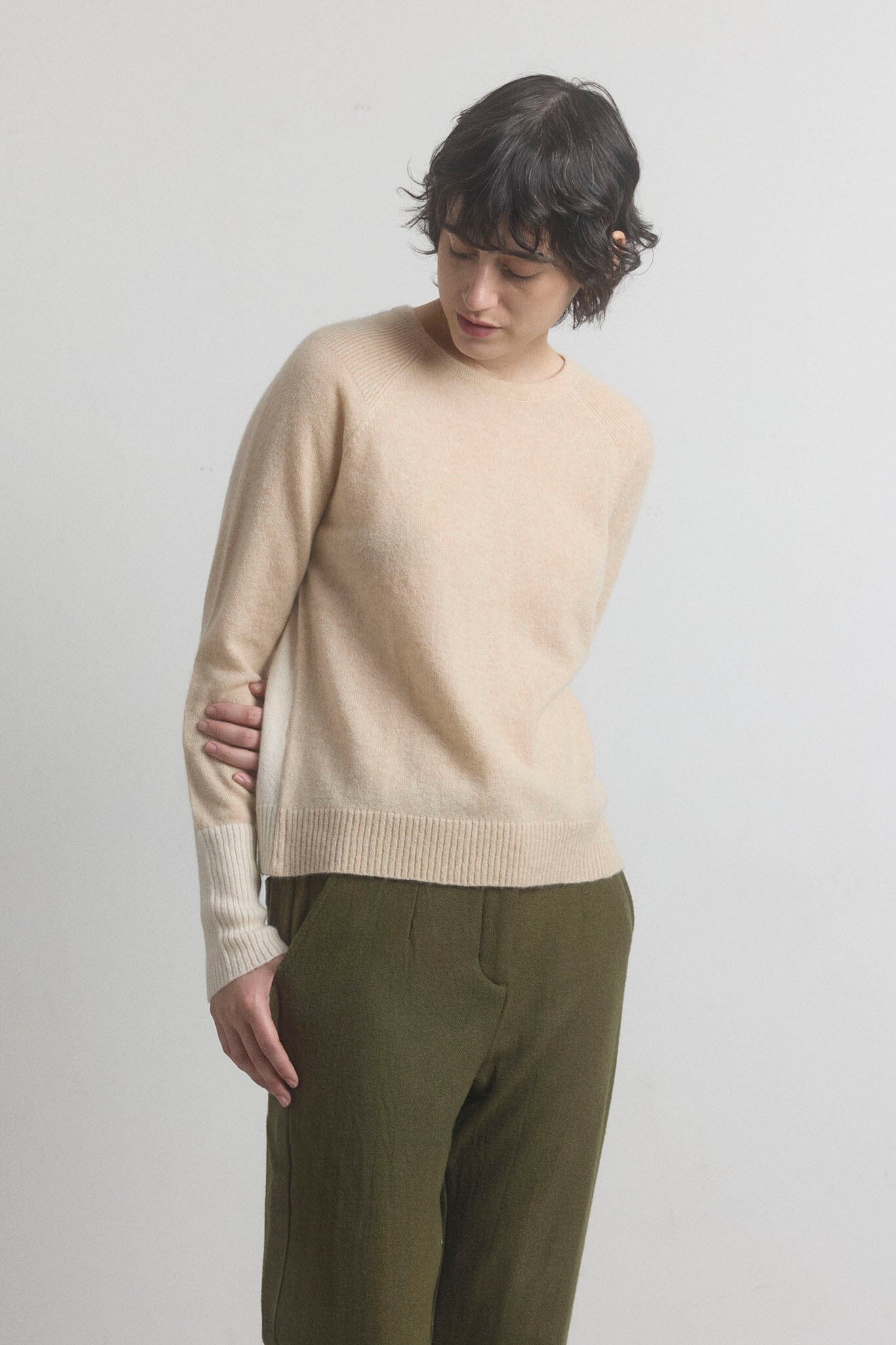 Woman wearing a beige cashmere sweater and green pants on a light gray background
