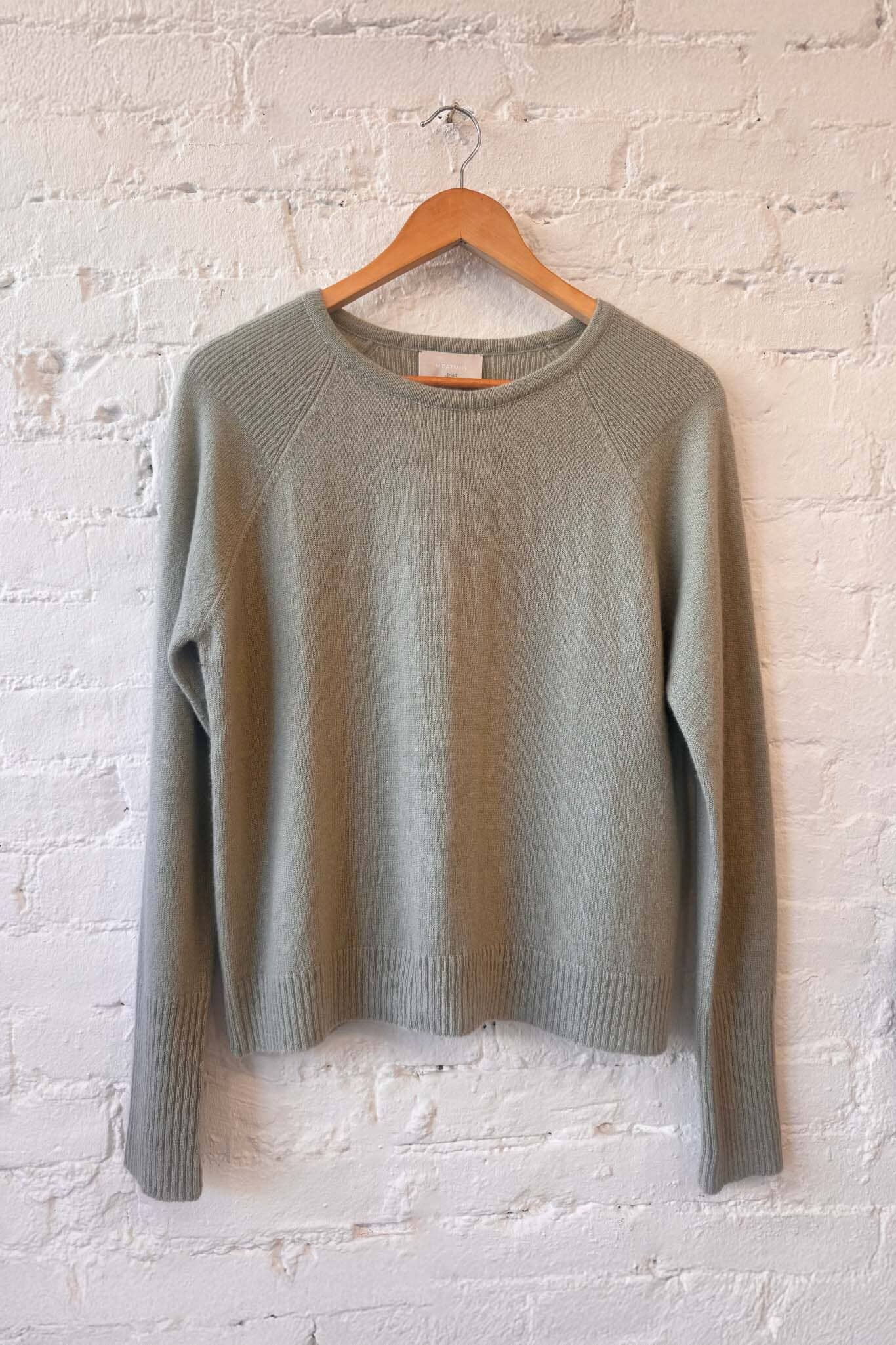 Sage green sweater on a wooden hanger against a white brick wall