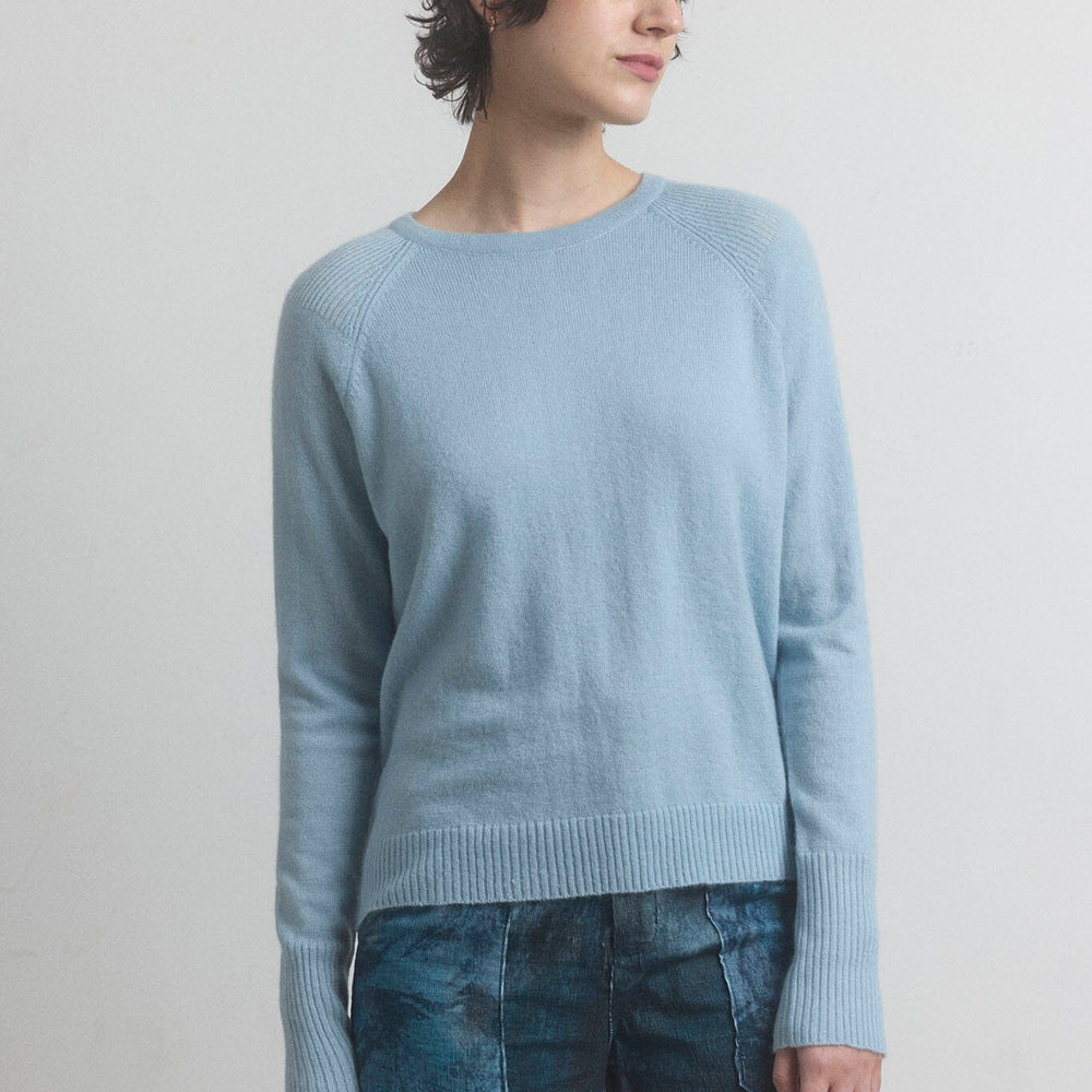 Woman wearing a light blue cashmere sweater and patterned pants against a plain background