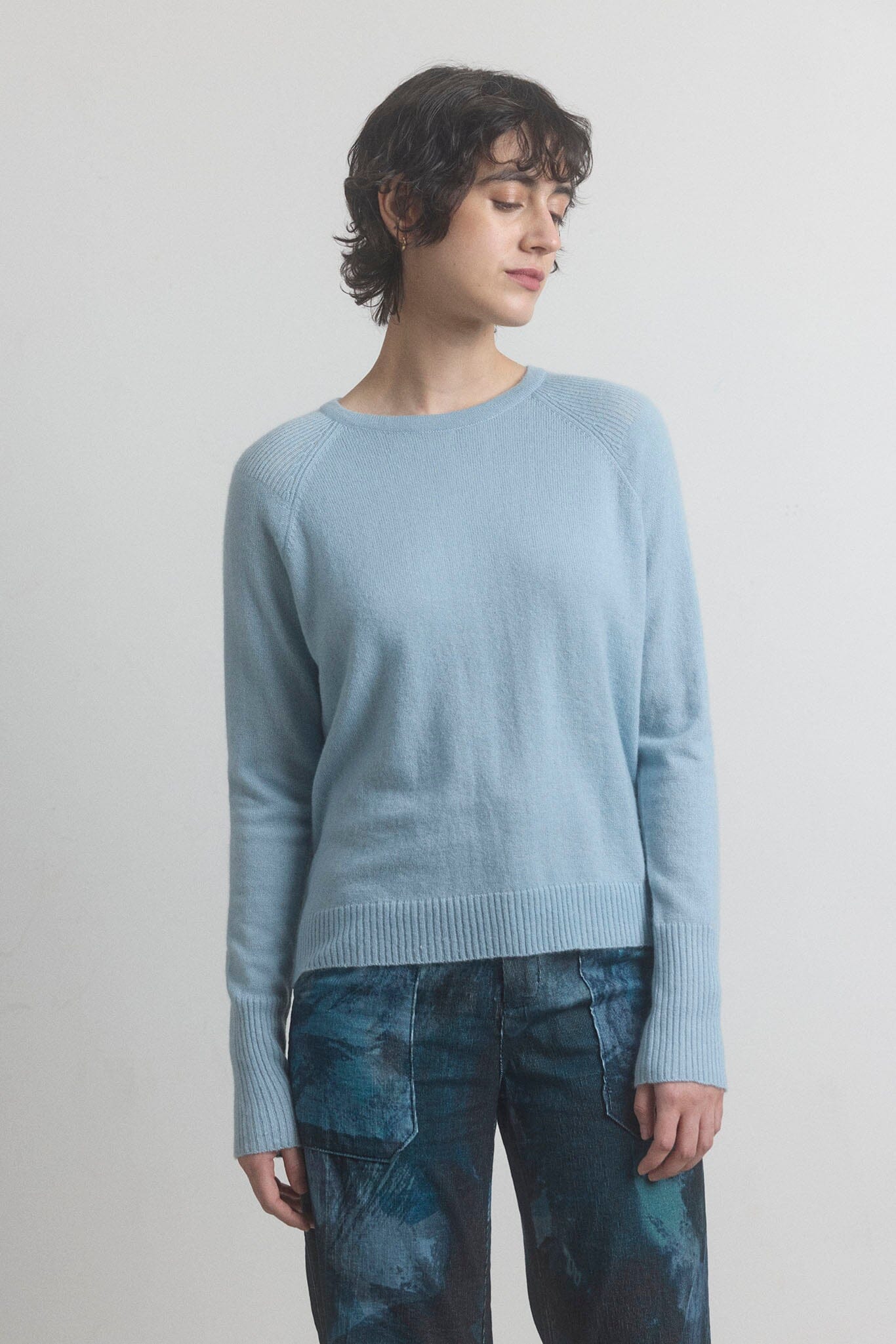 Woman wearing a light blue cashmere sweater and patterned pants against a plain background