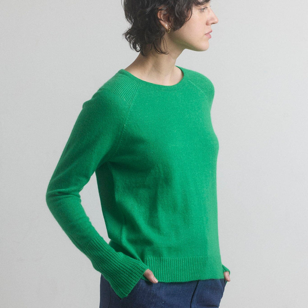Woman wearing a green sweater and blue pants against a plain background