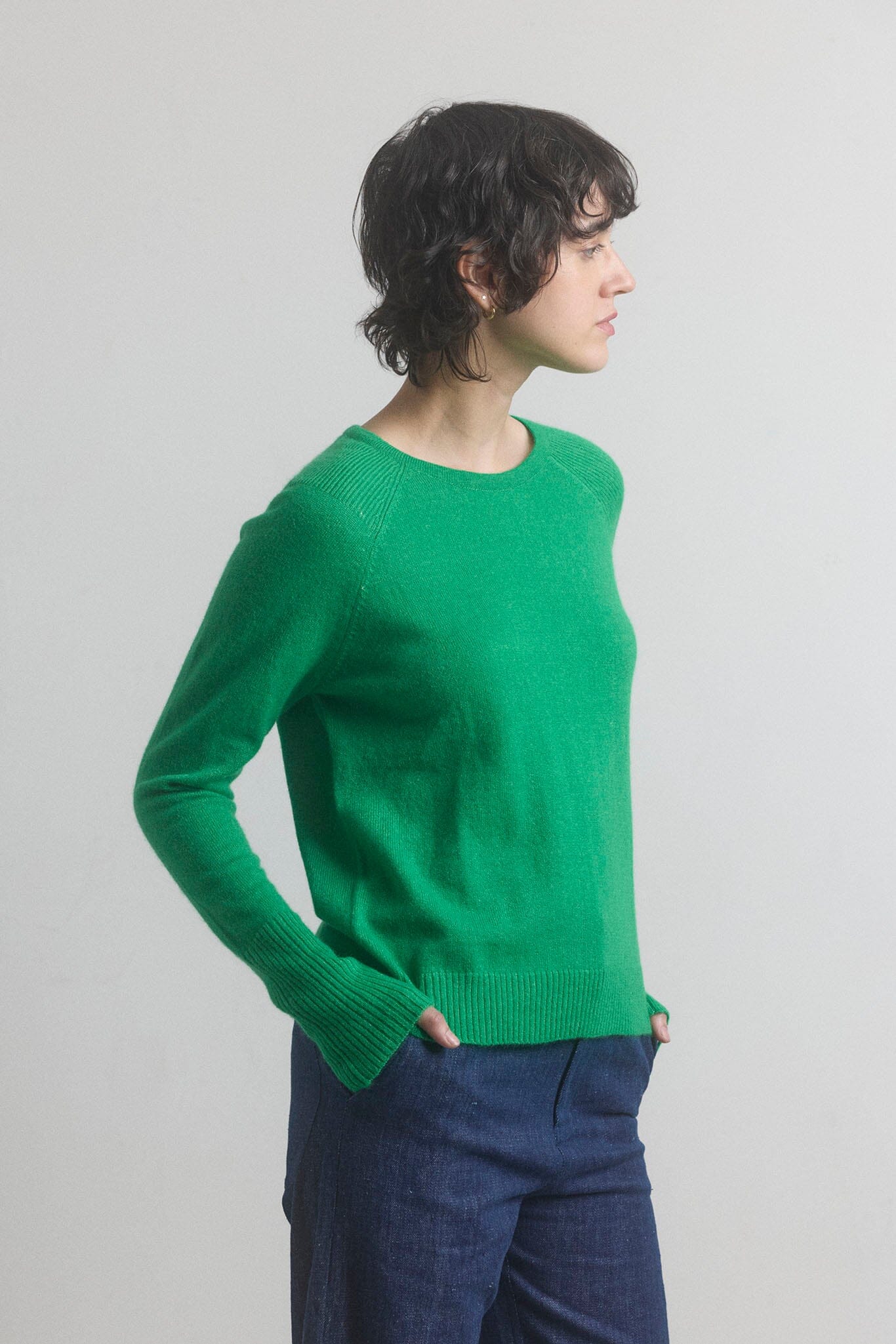 Woman wearing a green sweater and blue pants against a plain background