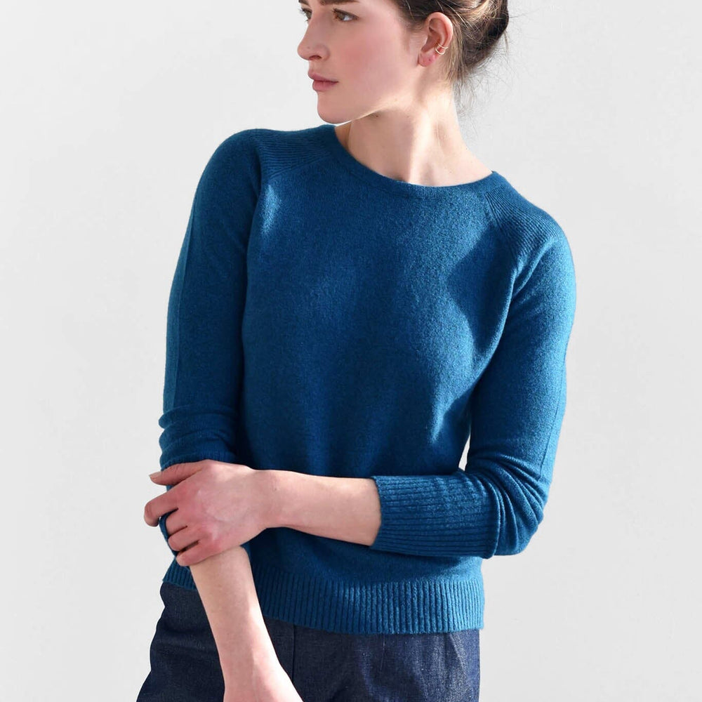 A woman wears the M.Patmos cashmere Brighton pullover sweater in a beautiful teal blue color. Designed in Brooklyn, New York.