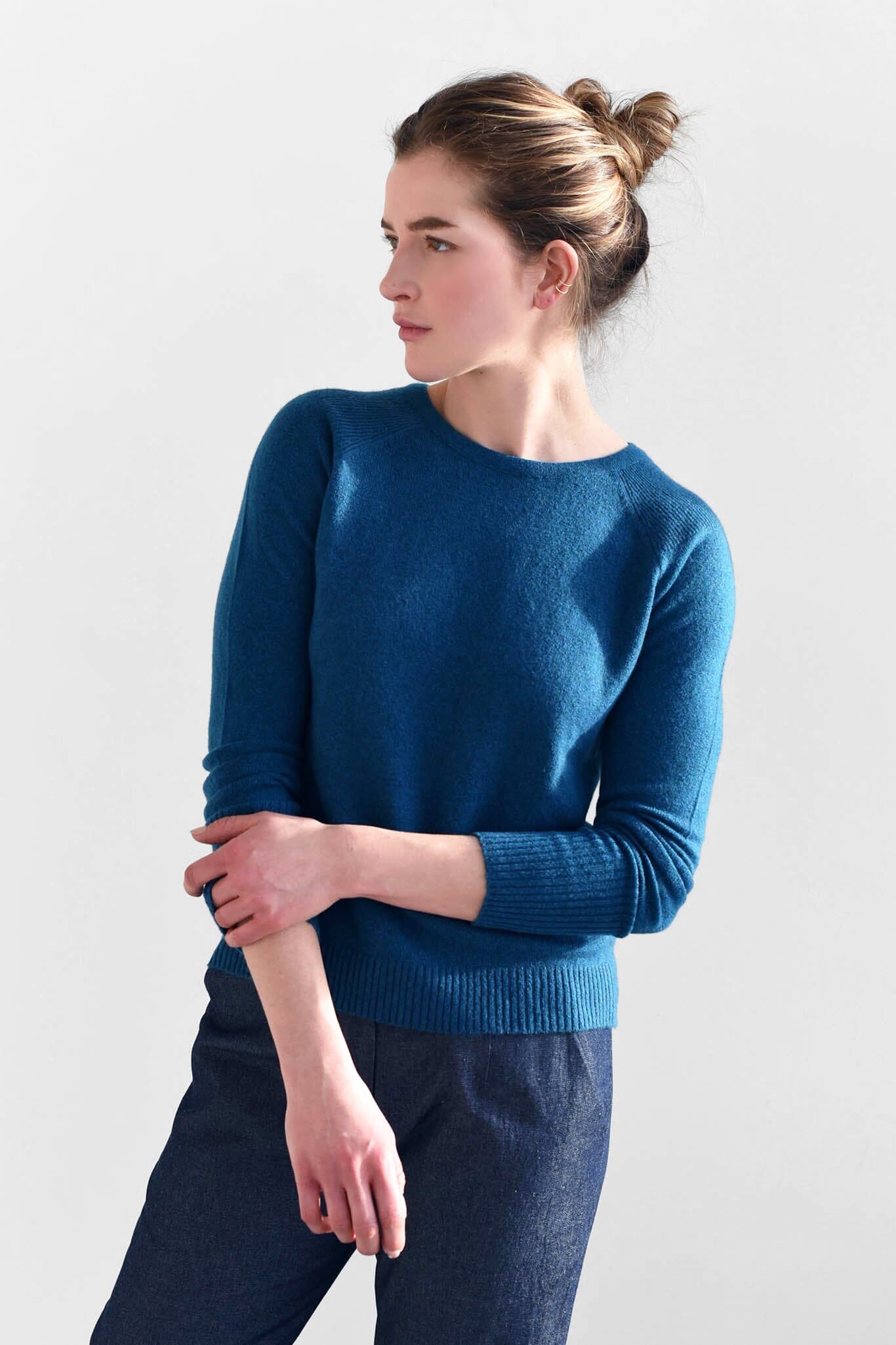 A woman wears the M.Patmos cashmere Brighton pullover sweater in a beautiful teal blue color. Designed in Brooklyn, New York.