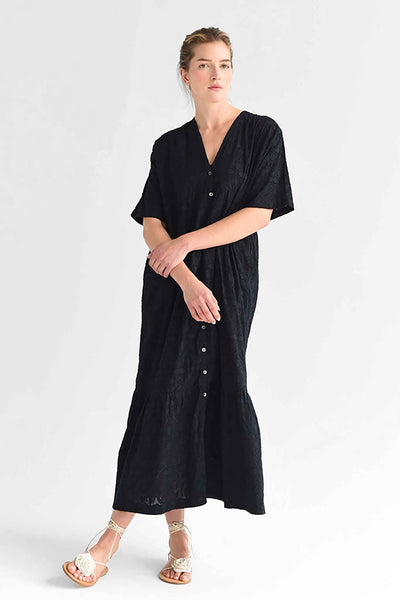 A woman wears the M.Patmos 100% cotton Linden dress featuring a floral jacquard fabric and buttons lining the front. Designed in Brooklyn, New York.