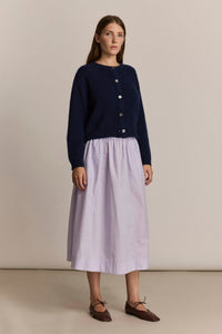 Woman wearing a navy cardigan and light purple skirt on a beige background