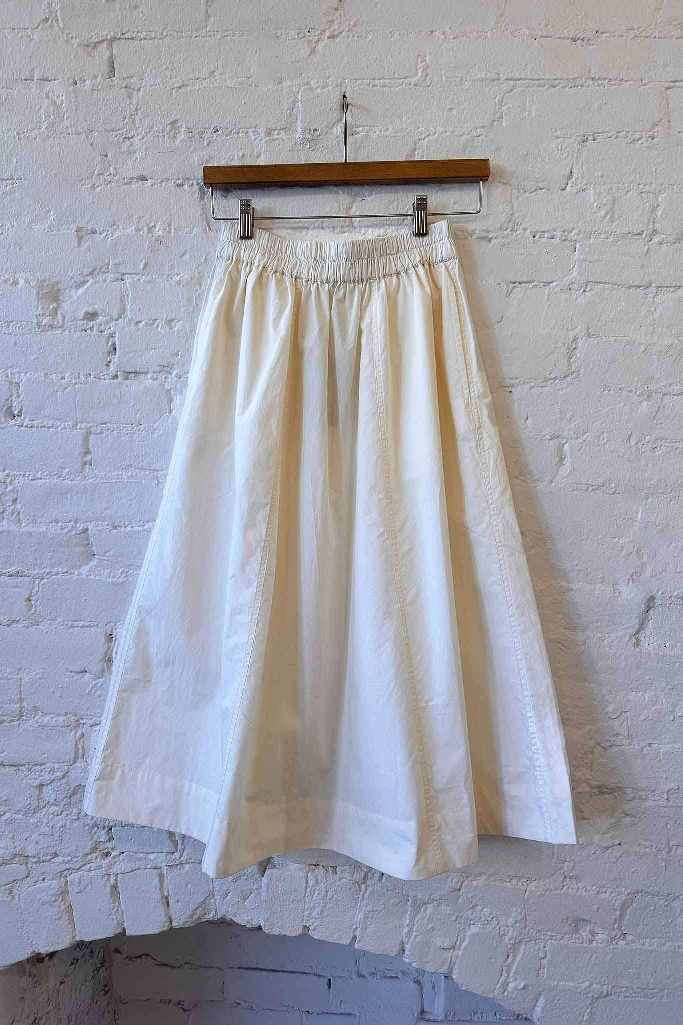 White skirt hanging on a wooden hanger against a white brick wall.