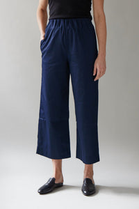 Person wearing navy blue pants and black shoes on a plain background