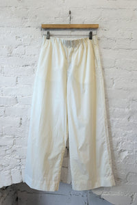 White pants hanging on a wooden hanger against a white brick wall.
