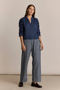 Woman wearing a navy blue blouse and striped denim pants against a beige background