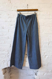 Blue striped pants hanging on a wooden hanger against a white brick wall.