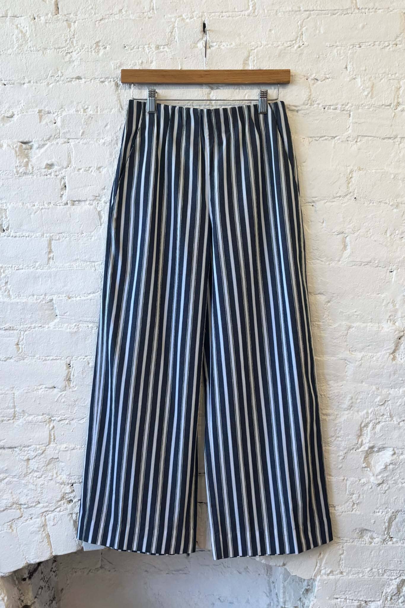 Navy and white striped pants hanging against a textured white brick wall.