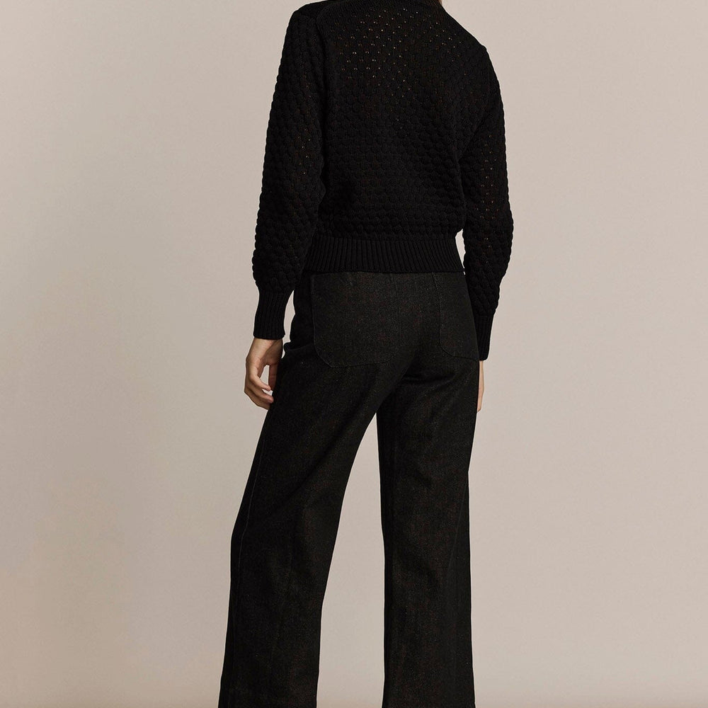 Person wearing a black sweater and pants against a beige background