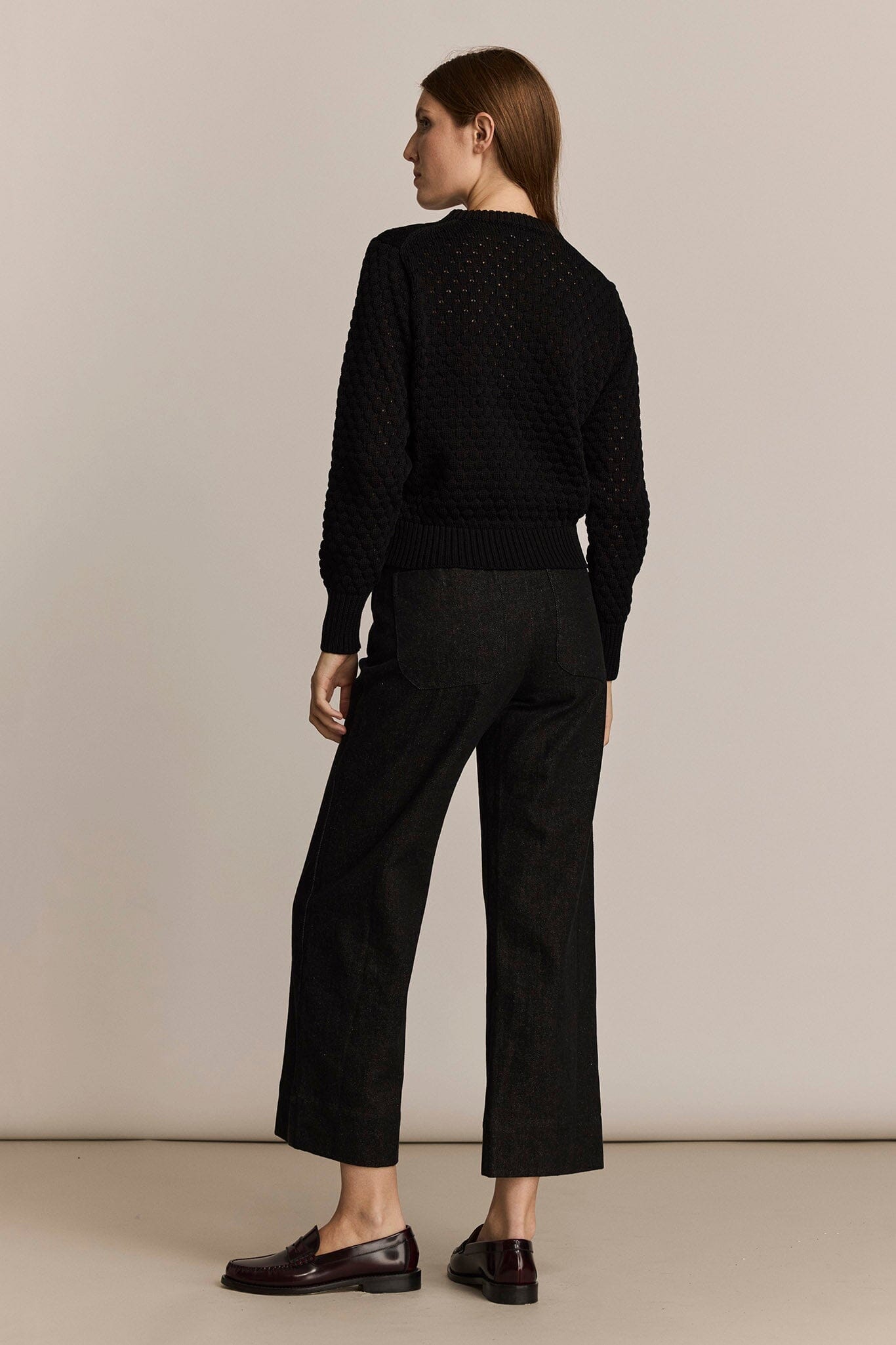Person wearing a black sweater and pants against a beige background
