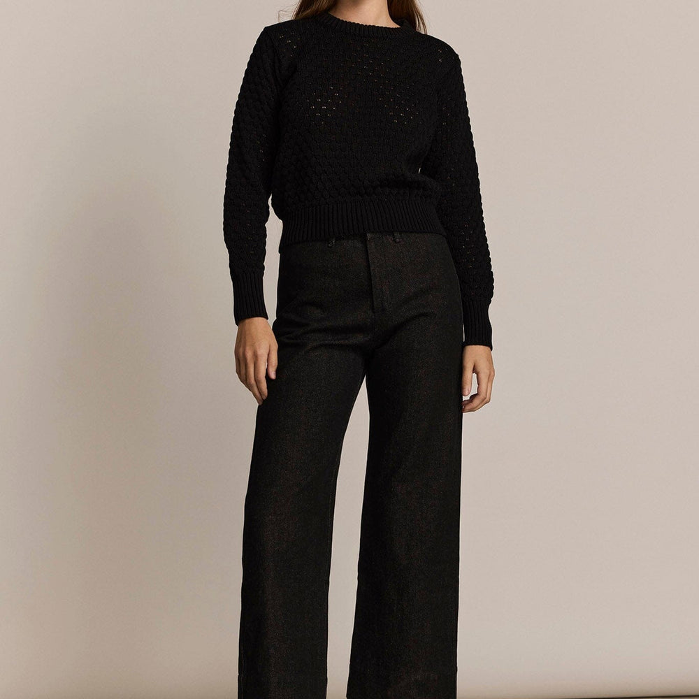 Woman wearing a black sweater and black denim pants against a beige background