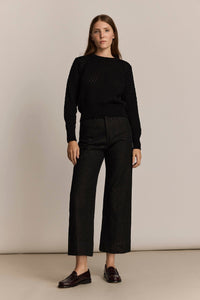 Woman wearing a black sweater and black denim pants against a beige background