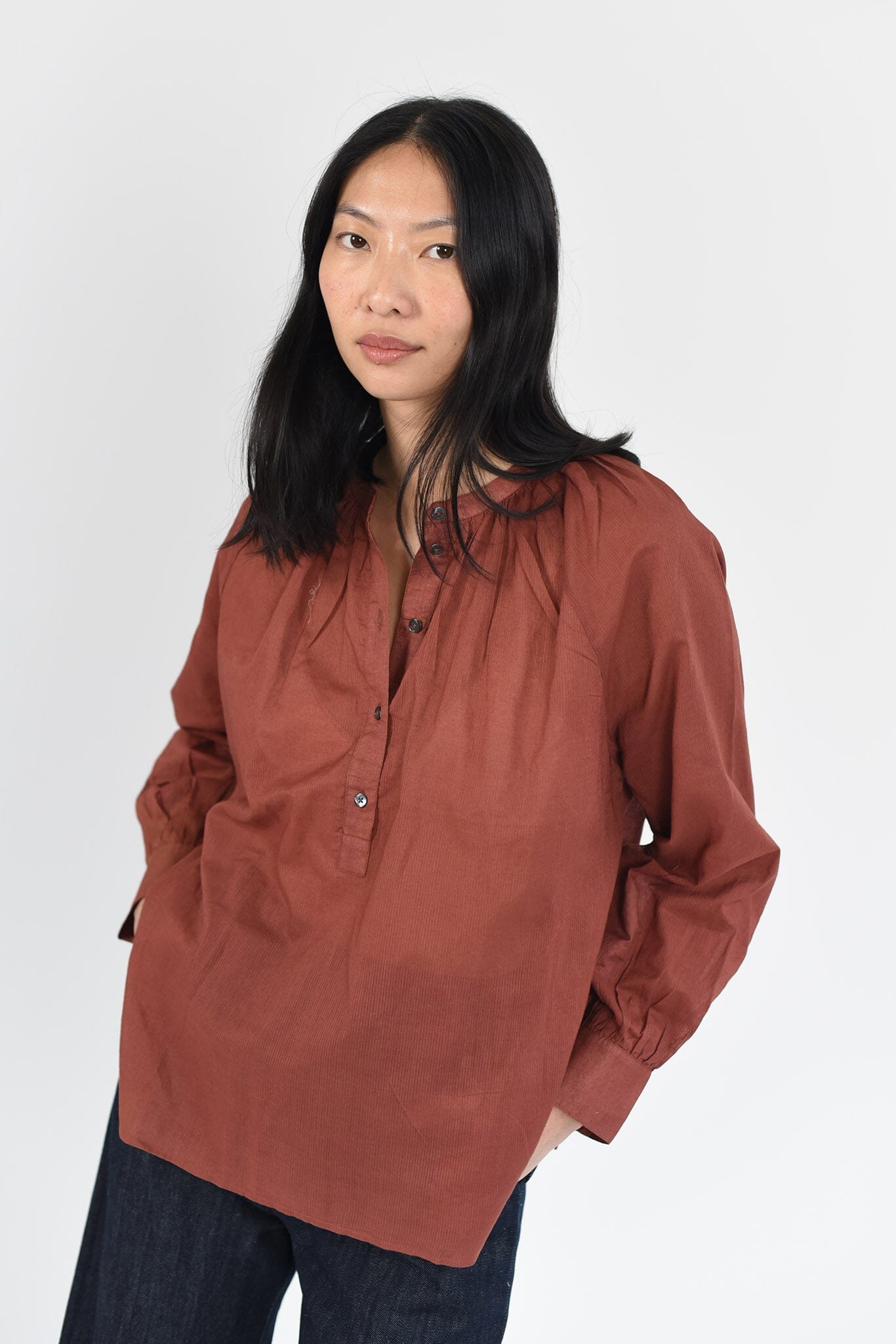 A woman wears a long sleeve, cotton blouse in a rich terracotta color. Designed by Brooklyn womensware brand, M.Patmos.