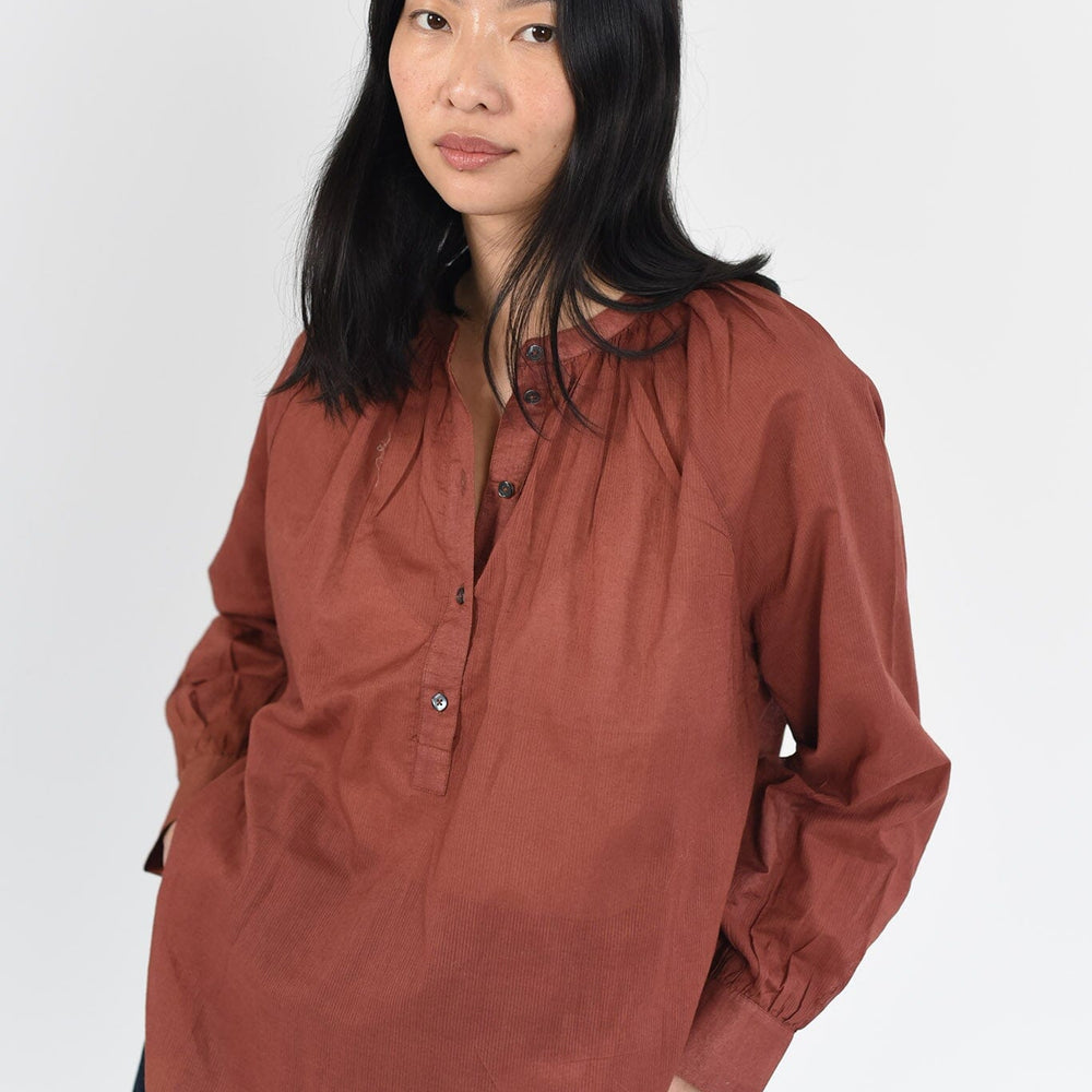 A woman wears a long sleeve, cotton blouse in a rich terracotta color. Designed by Brooklyn womensware brand, M.Patmos.