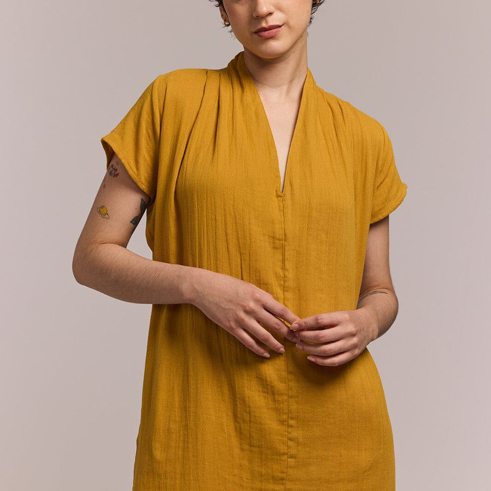 Woman wearing a mustard cotton yellow dress against a plain background