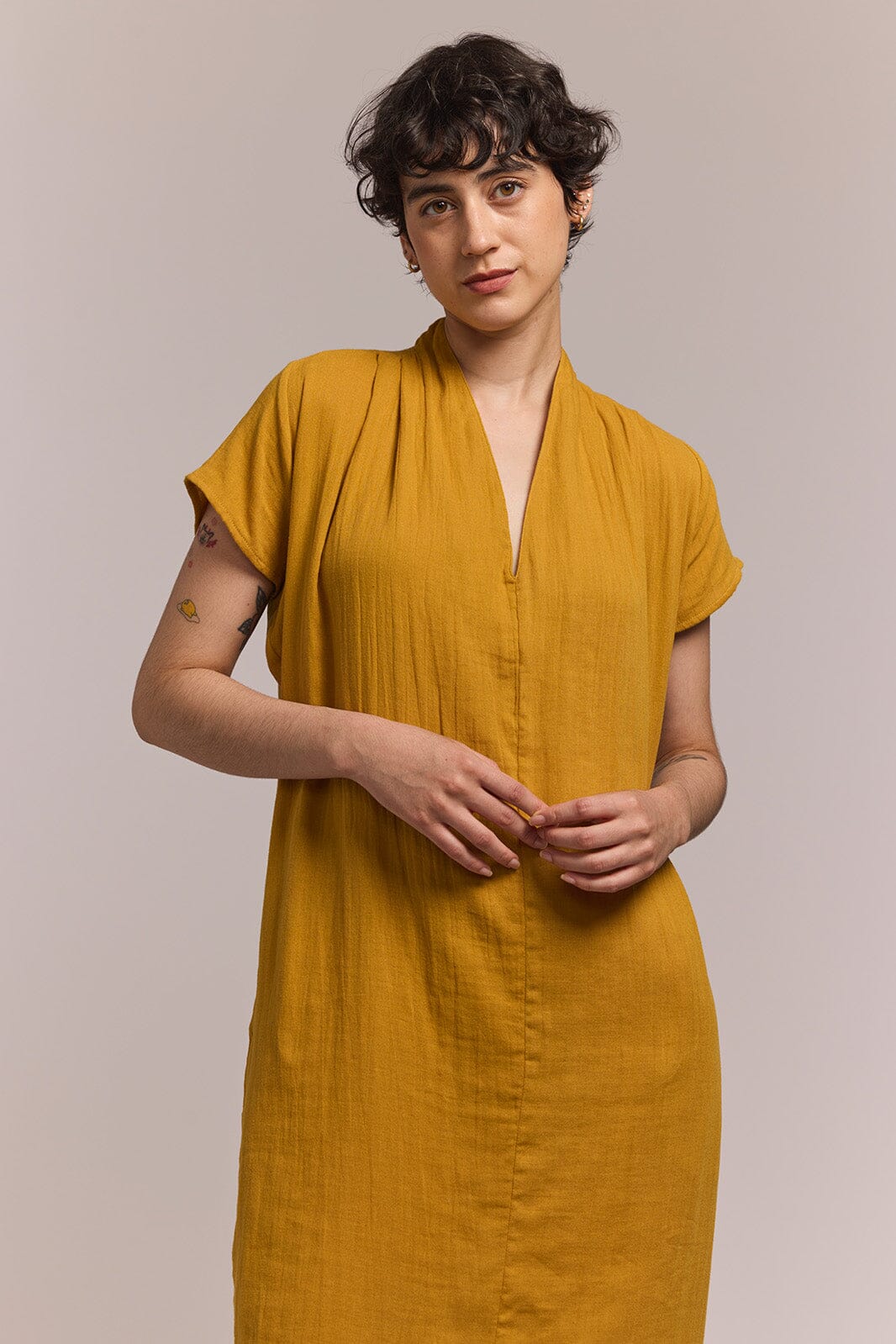 Woman wearing a mustard cotton yellow dress against a plain background