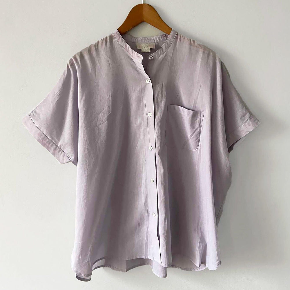 A lavender colored short sleeve blouse with a button-up front displayed on a hanger against a white background.