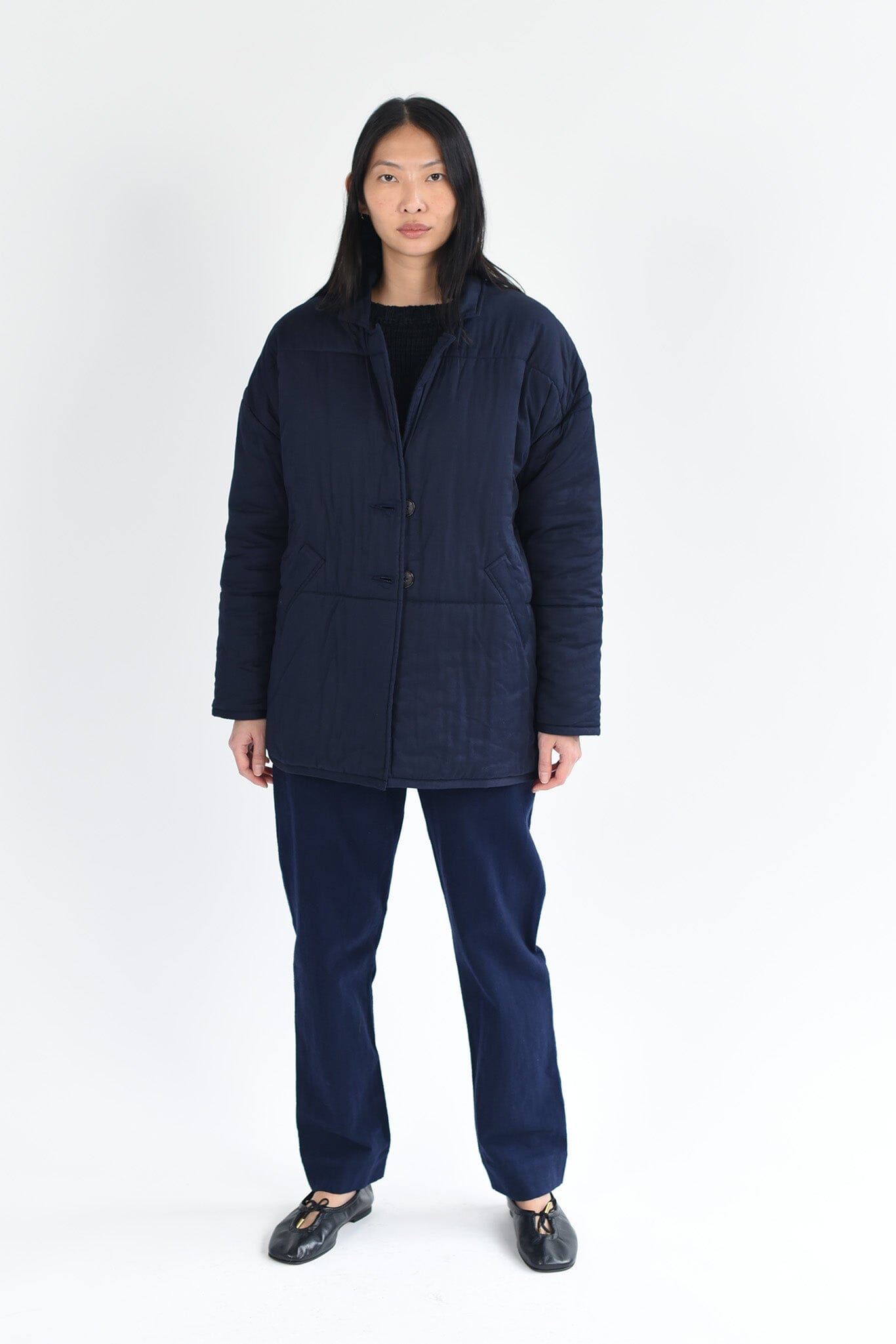 A woman wears the M.Patmos navy blue Haven quilted, long sleeve coat. Two pockets and buttons down the front.