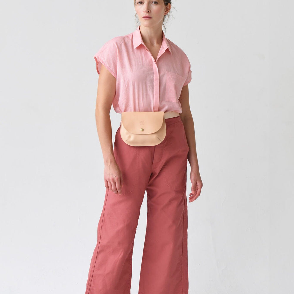 
                  
                    A woman wears a pink short sleeve top with a beige crossbody leather bag.
                  
                