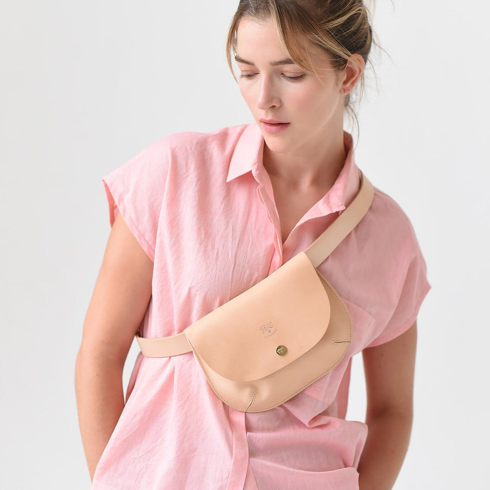 A woman wears a beige leather crossbody bag with a snap closure.