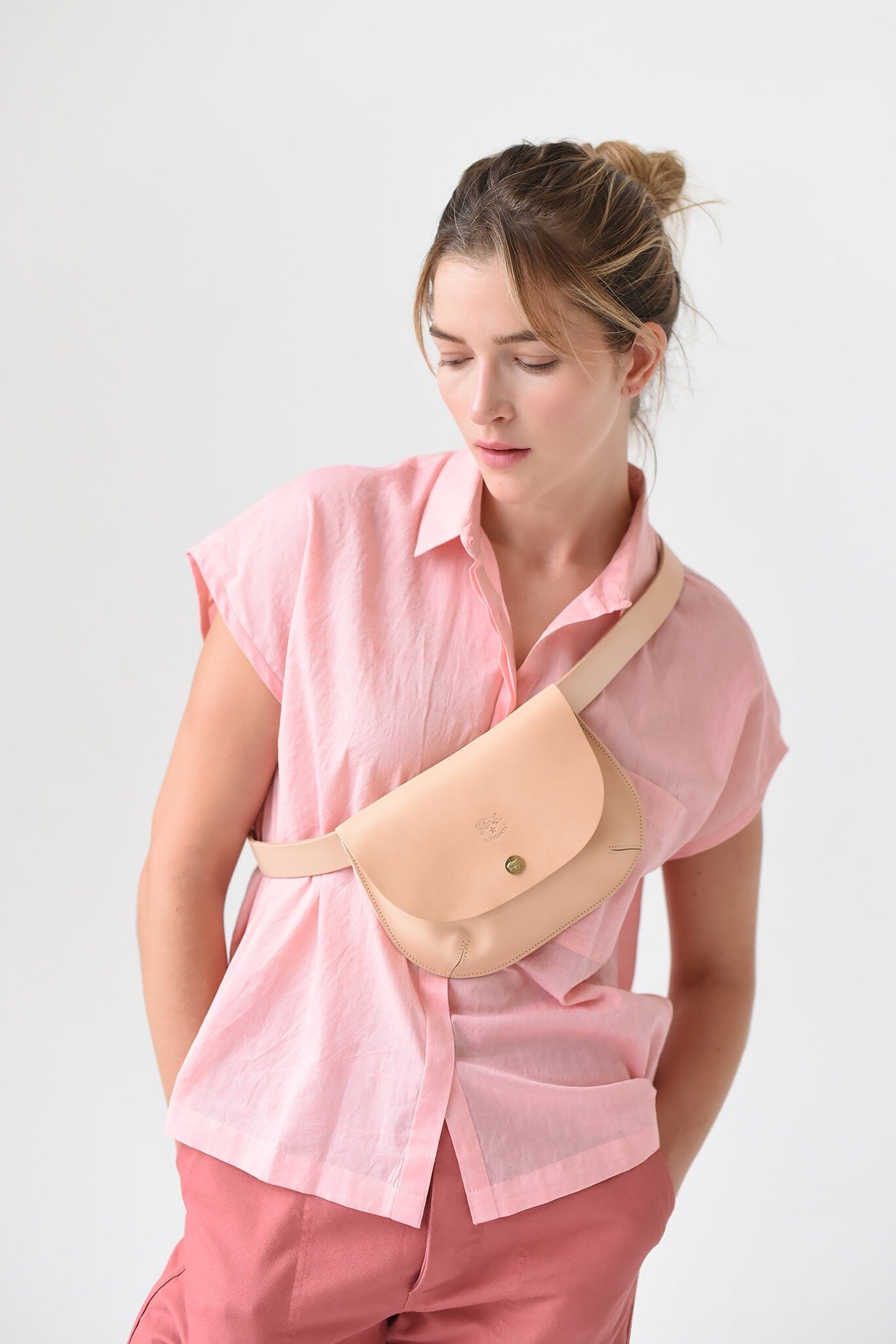 A woman wears a beige leather crossbody bag with a snap closure.