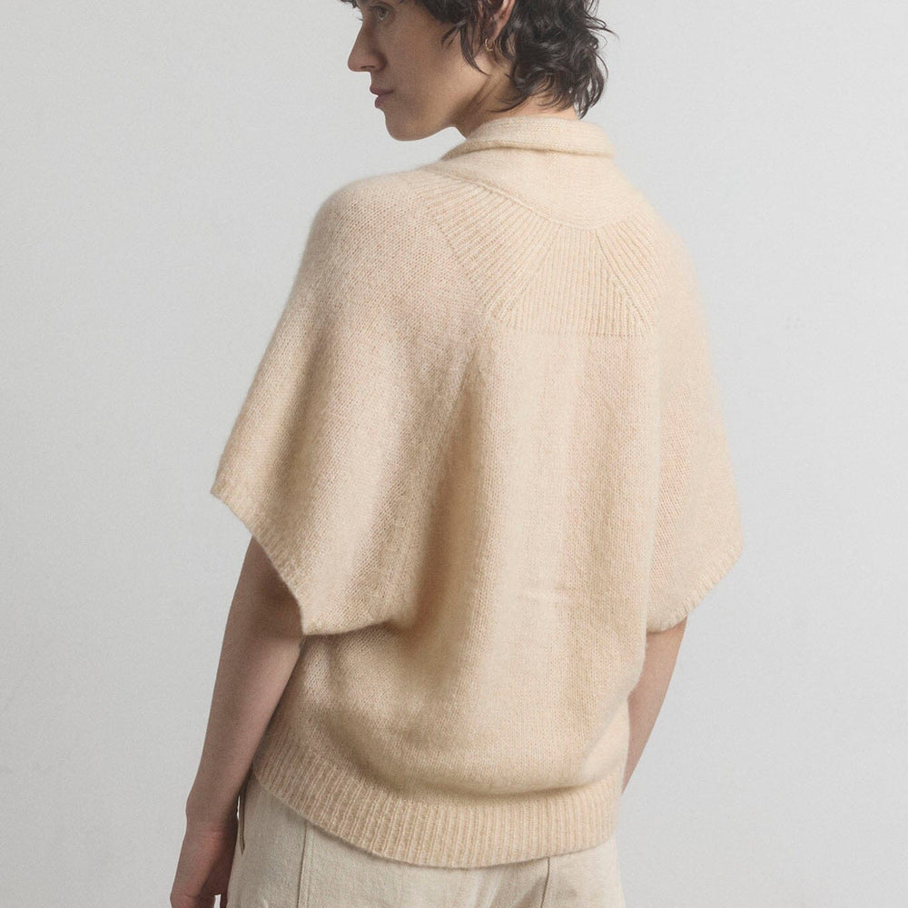 Person wearing a beige cashmere cardigan and pants against a plain background