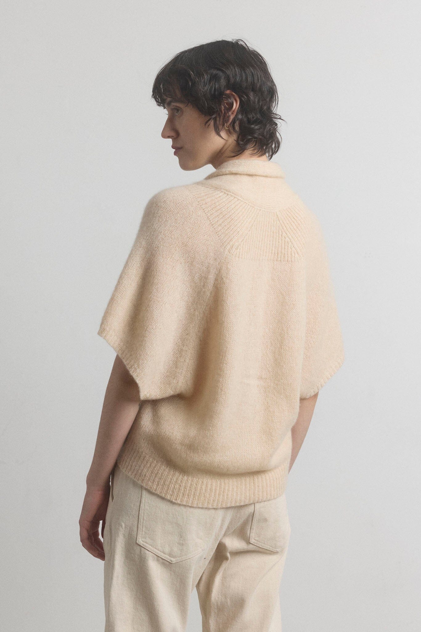 Person wearing a beige cashmere cardigan and pants against a plain background