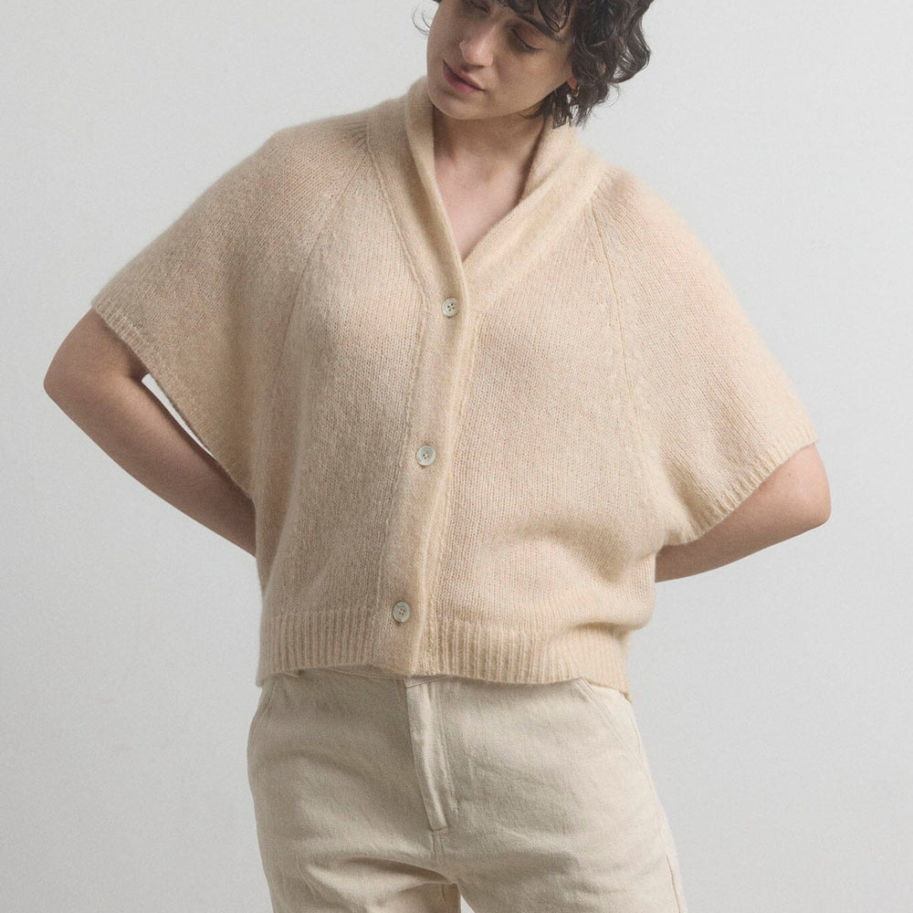Person wearing a beige cashmere cardigan and pants against a plain background