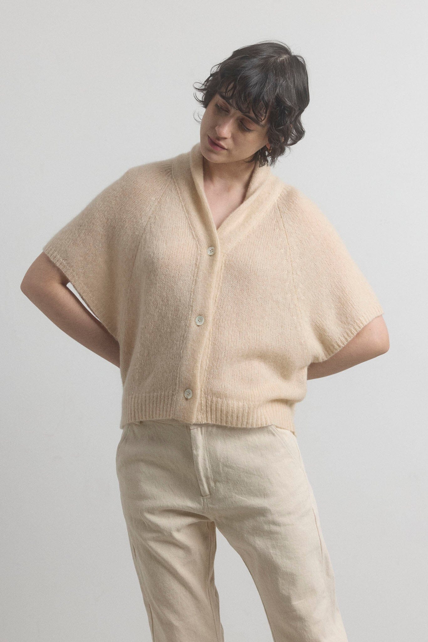 Person wearing a beige cashmere cardigan and pants against a plain background