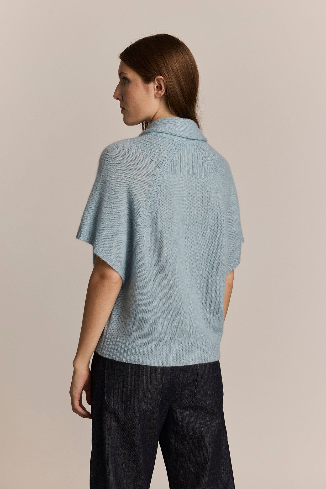 Woman wearing a light blue cashmere knit short sleeved sweater against a beige background