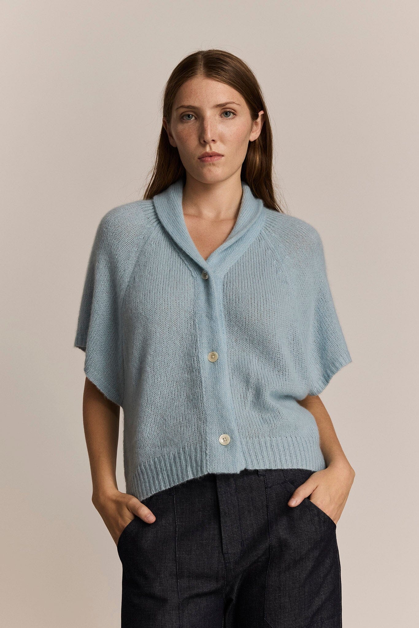 Woman wearing a light blue cashmere cardigan with denim pants against a beige background