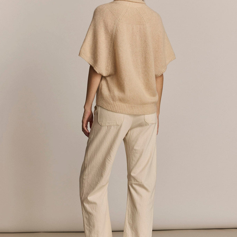 Person wearing a beige short sleeve soft sweater against a plain background