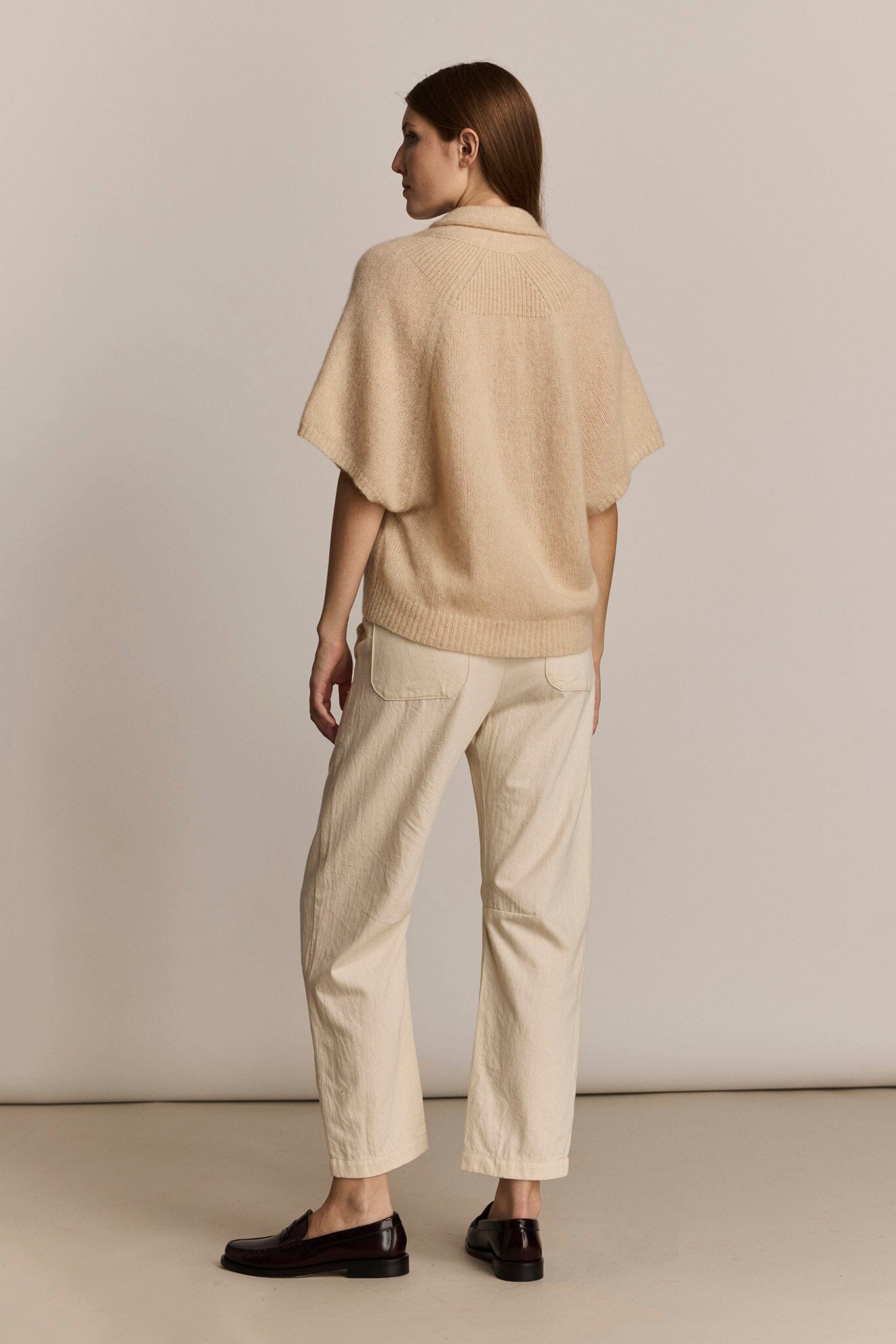 Person wearing a beige short sleeve soft sweater against a plain background