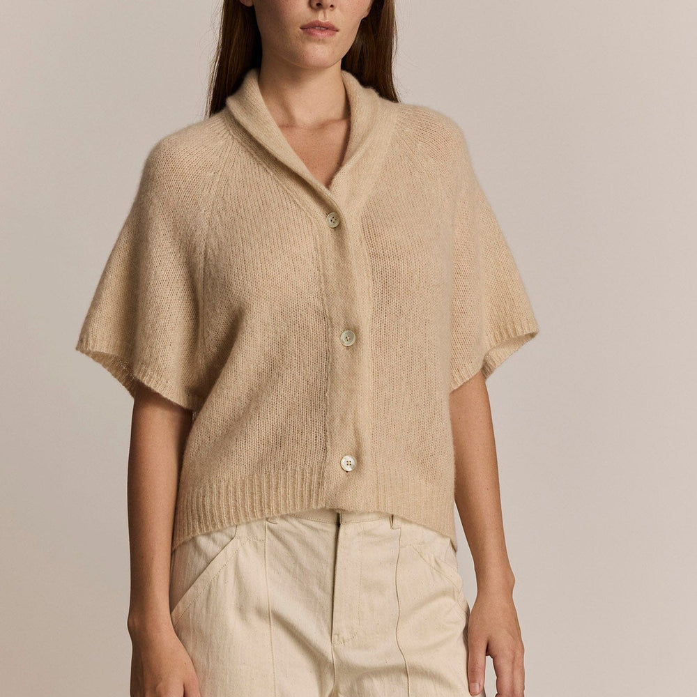 Woman wearing a beige short sleeve knit cardigan and pants against a plain background